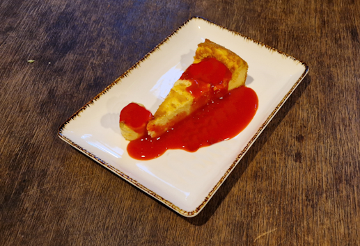 hauseigener käsekuchen-cheesecake mit schokoflecken auf einer weißen rechteckigem desserttellerauf einem alten holztisch