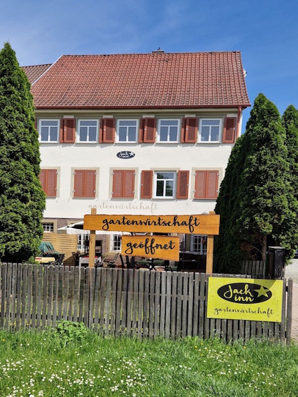 Sommerliche Gartenwirtschaft des Jack Inn mit Holztischen und Pflanzen