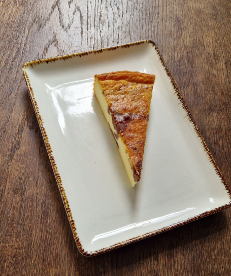 hauseigener käsekuchen-cheesecake mit schokoflecken auf einer weißen rechteckigem desserttellerauf einem alten holztisch