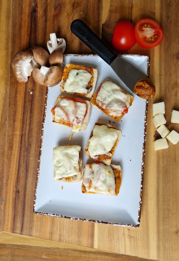 miniciabattahälften belegt mit tomate und champignons überbacken mit käse, als deko käsewürfel,
                halbierte tomate, champignons und ein spatel mit tomatenpesto. auf einem schönen holzbrett