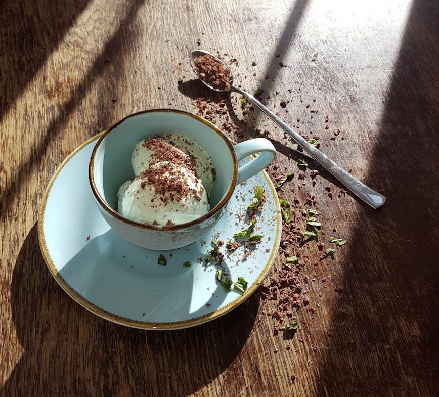 hausgemachtes minzeis mit geraspelten schokochips aus fairtrade schokolade 60% in einer blaumellierten kaffeetasse auf einem alten holztisch. 
                deckoriert mit schokochips und gehackter frischer minze