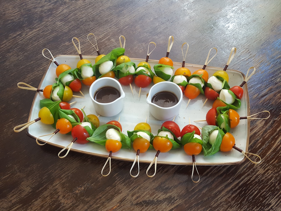 tomaten-mozarella spiesschen mit mini mozarella und mini tomaten dazwischen basilikumblätter.
                auf einer platte im kreis gelegt, in der mitte 2 kleine ausgiesser mit balsamicodressing.
                auf einem alten holztisch