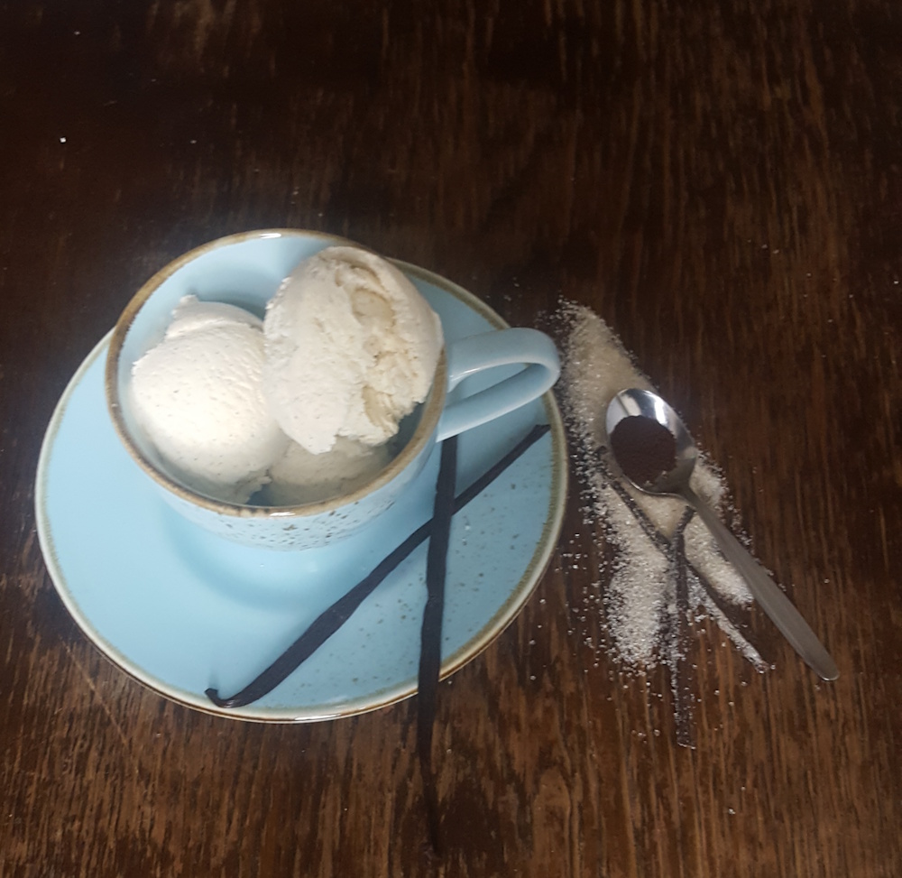 hausgemachtes vanilleeis, in einer blaumellierten kaffeetasse. deko vanilleschoten, vanillepulver auf einem teelöffel,
                selbstgemachter vanillezucker. die tasse steht auf einem alten holztisch